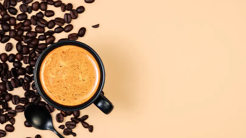 An image of a cup of coffee and some coffee beans on a table