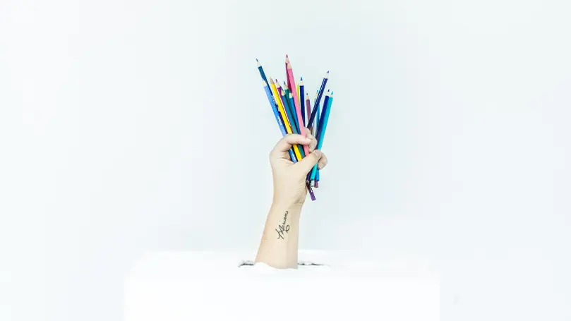 An image of a hand holding many different coloured pencils