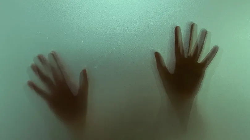 A nightmarish scene of two hands being pressed upon green glass