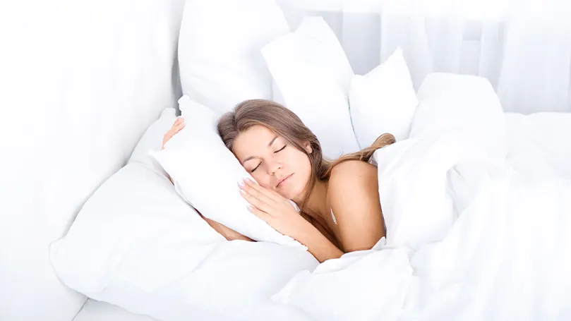 An image of a woman sleeping with a large number of pillows