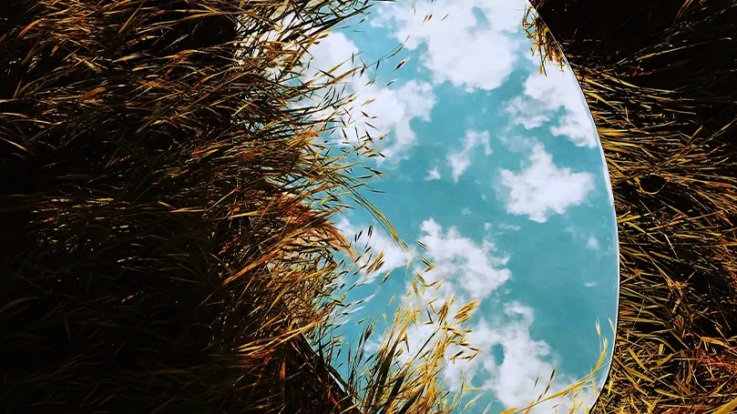An image of a mirror laid on the ground reflecting the sky