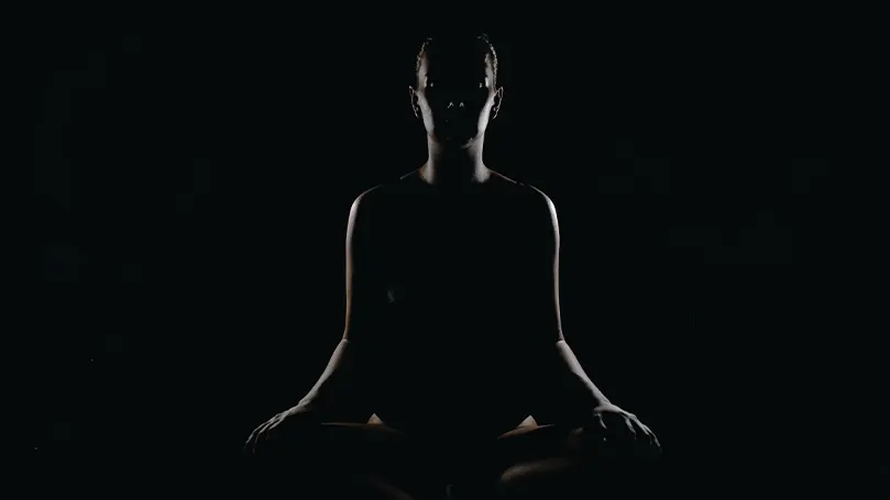 An image of a person meditating in a darky lit room