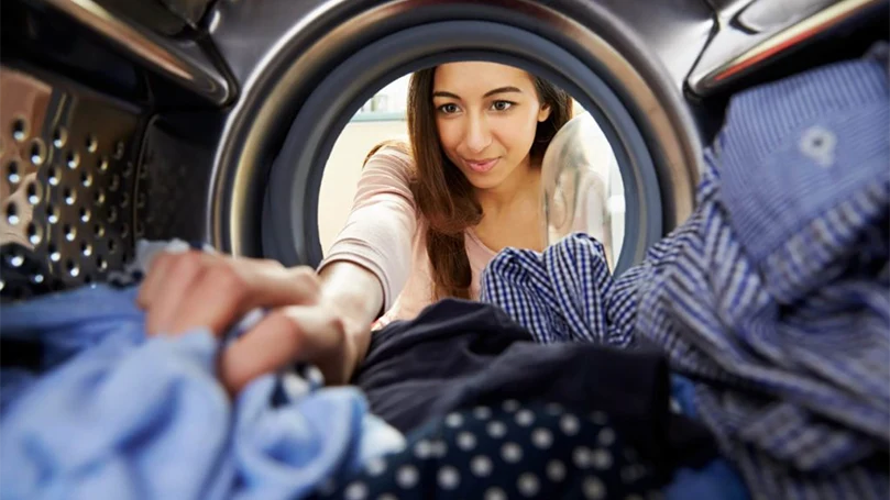 an image of a woman putting clothes in the washing machine