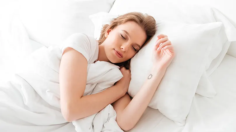 An image of a woman sleeping comfortably under a warm duvet