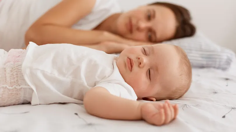 An image of a baby sleeping next to mom.