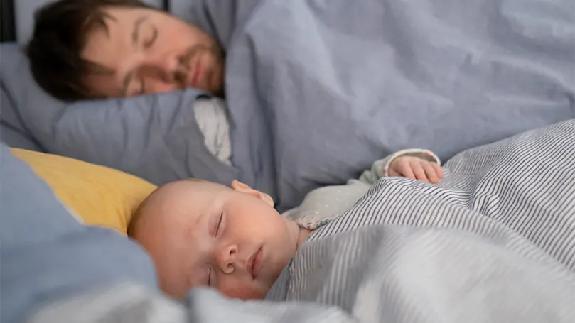 An image of a baby sleeping next to dad.