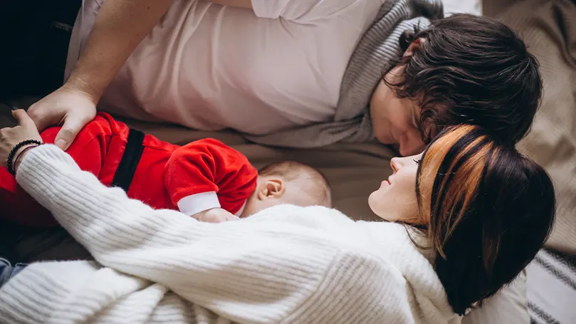 An image of a baby sleeping between parents.