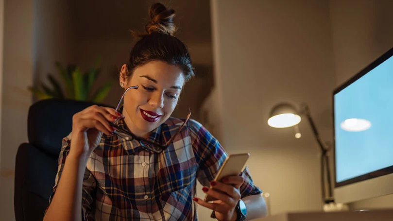 an image of a woman holding her phone in front of a computer