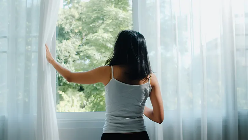 An image of a woman opening the window and letting fresh air in