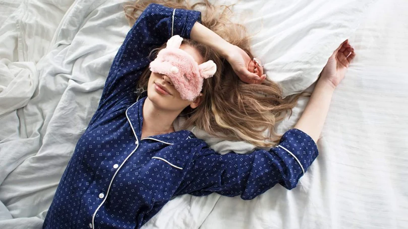a woman sleeping with an eye mask on her back