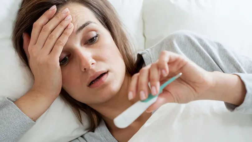 a sick woman with a fever holding a thermometer