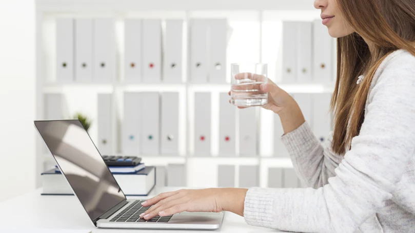 a woman drinks a glass of water while working