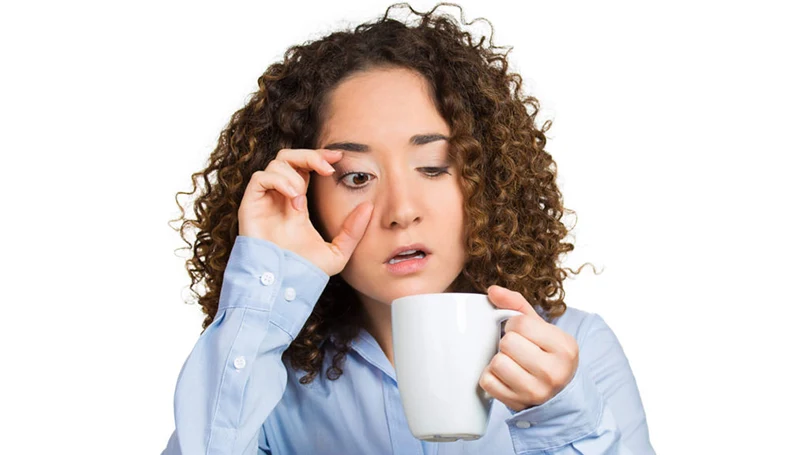an image of a woman waking up groggy and drinking a cup of coffee