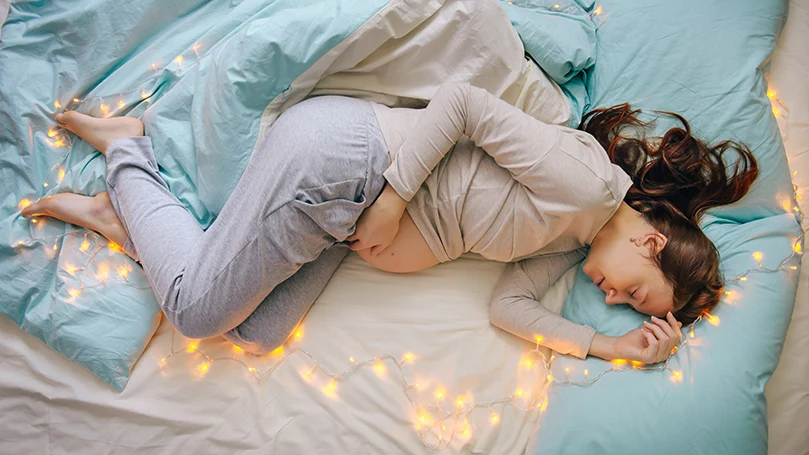 an image of a pregnant woman sleeping in a bed with the lights on