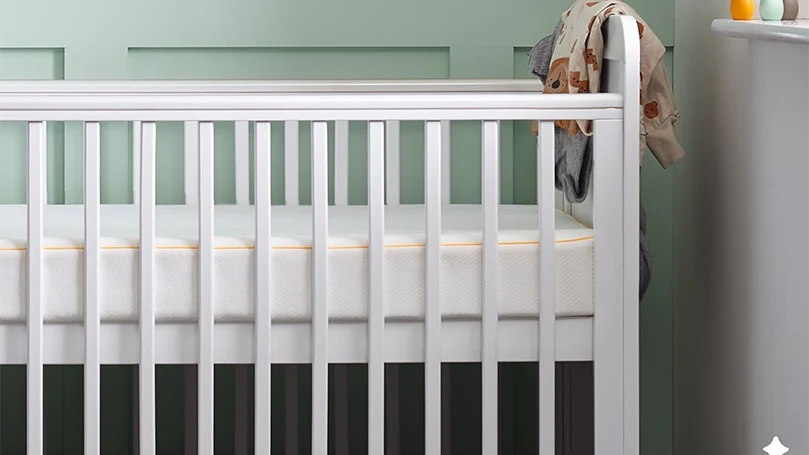 An image of Eve cot baby mattress in the corner.