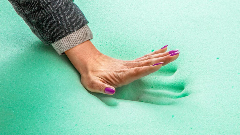 A hand touching memory foam on a mattress