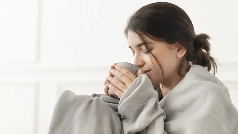 An image of a woman drinking tea wrapped in a weighted blanket for deep pressure stimulation.