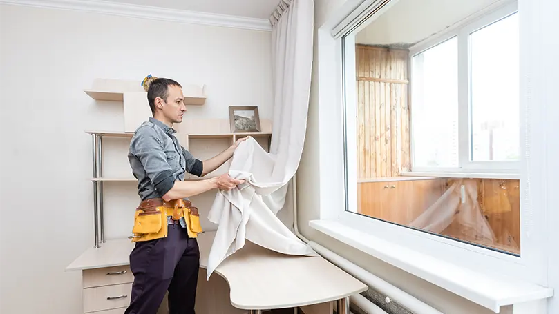 An image of a handyman installing curtains.
