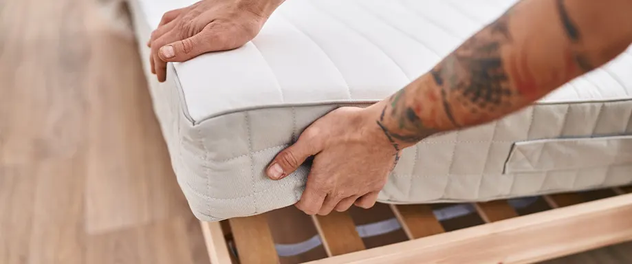 Man placing mattress on bed