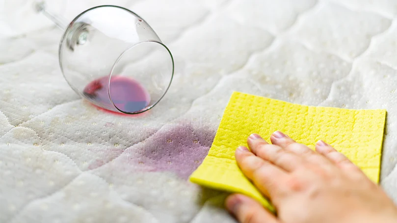 a woman blotting a wine stain on a mattress topper.