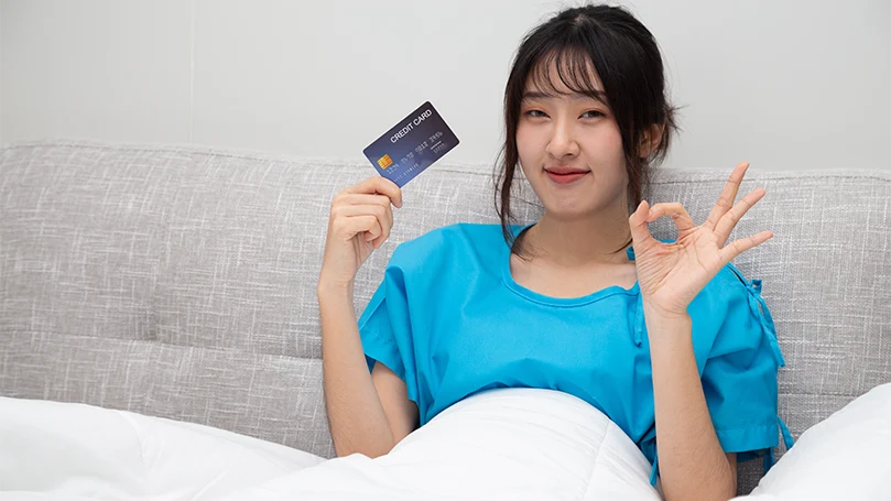 An Asian woman in bed holding her credit card