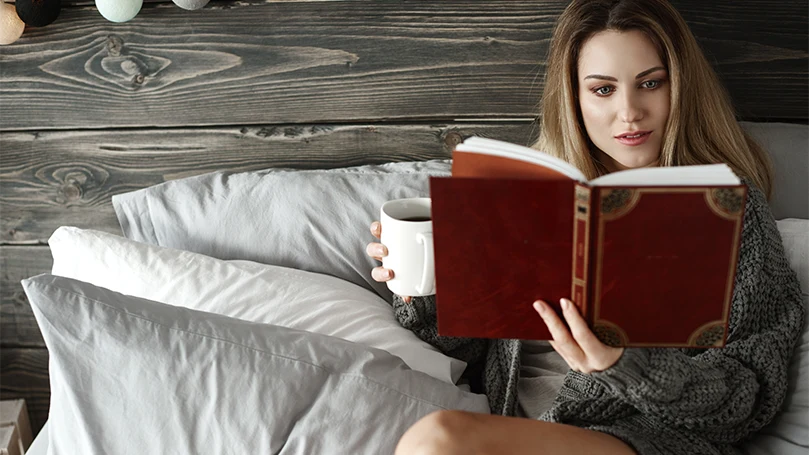 An image of a woman reading a book in bed