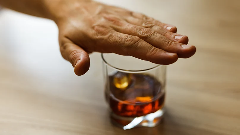 A male's hand over the glass of alcohol.