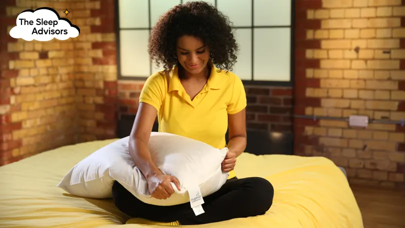 Our reviewer squeezing the Snuggledown Goose Feather and Down pillow while sitting on a bed