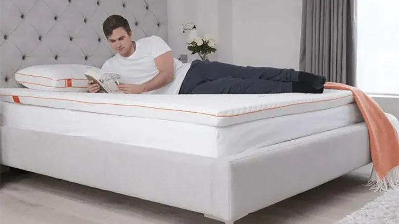 A man laying down on Dormeo Octasmart mattress topper reading a book.