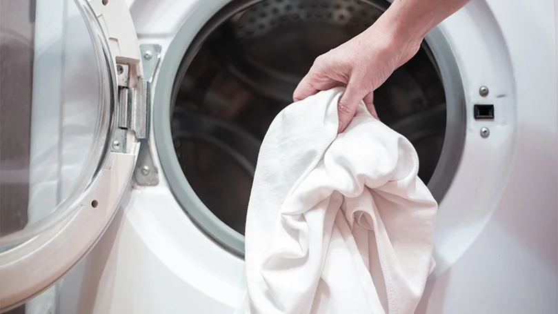 a man putting a pillowcase in a washing machine.