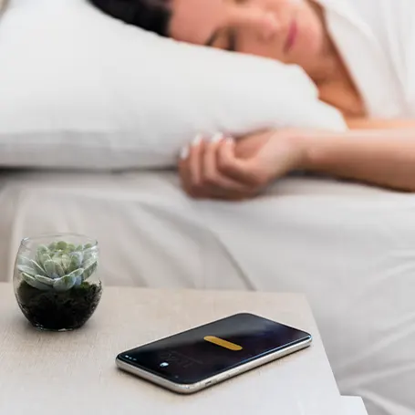 An image of a woman sleeping with her phone on the nightstand
