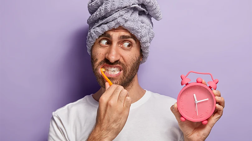 An image of a man who woke up late looking at a clock and washing his teeth