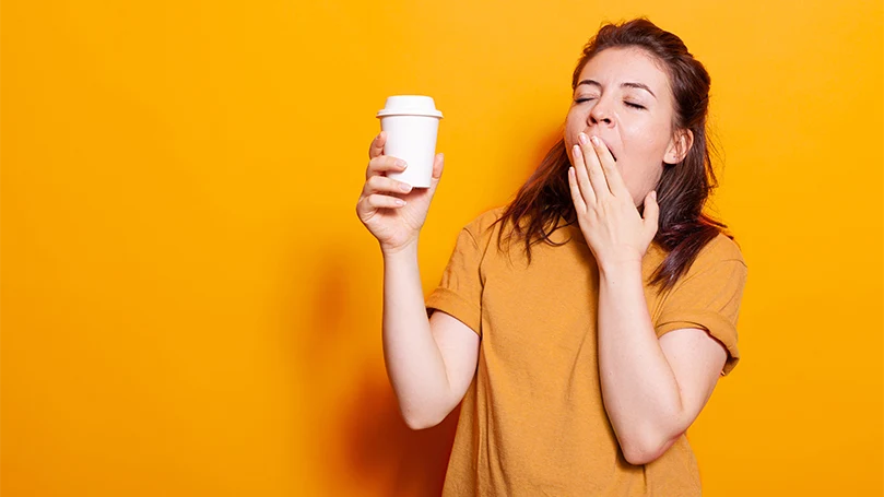An image of a sleepy woman holding a cup of coffee.