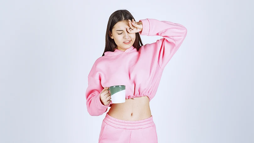 An image of a young woman in a pink pajama feeling sleepy.