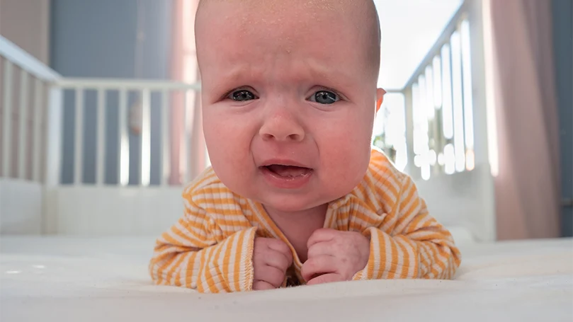 An image of a baby crying in a cot bed.