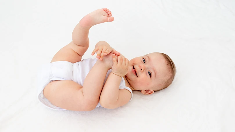 An image of a baby laying on back and smiling.