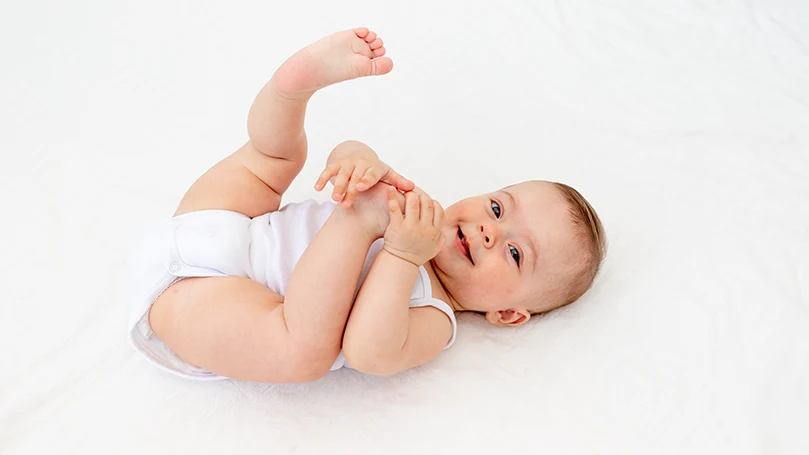 A baby laying on back and smiling.