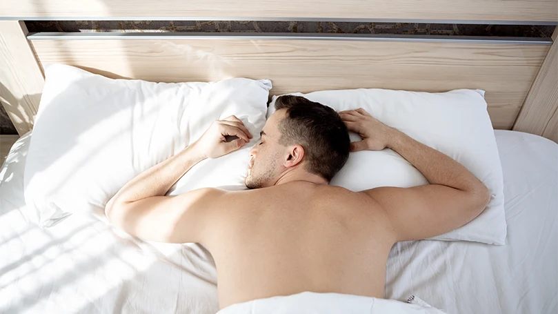 a man sleeping on stomach in his bed.