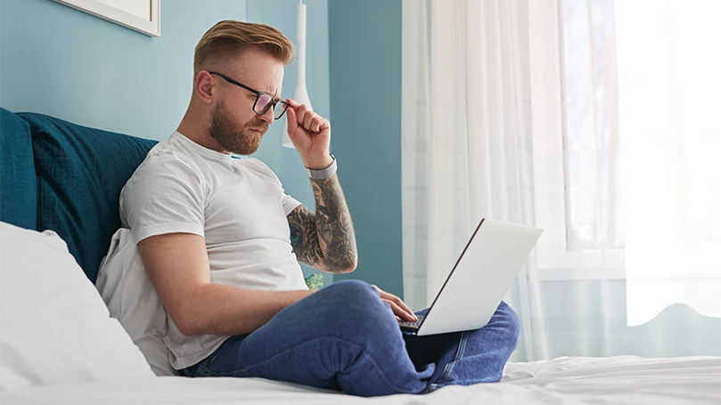 An image of a man working from home in his bed.