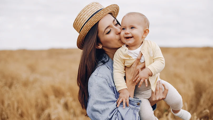 An image of a mom holding her baby in the field.