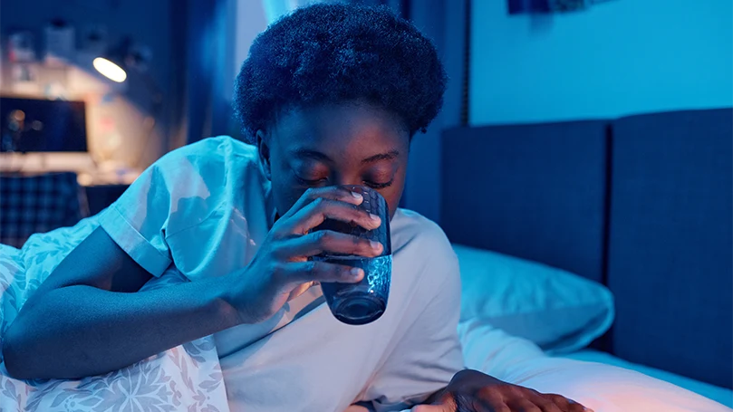 An image of a woman drinking a glass of water before the bed time.
