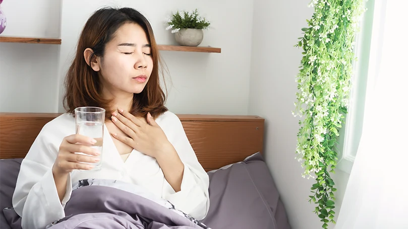 An image of a young and sick asian woman drinking water in bed before sleep.