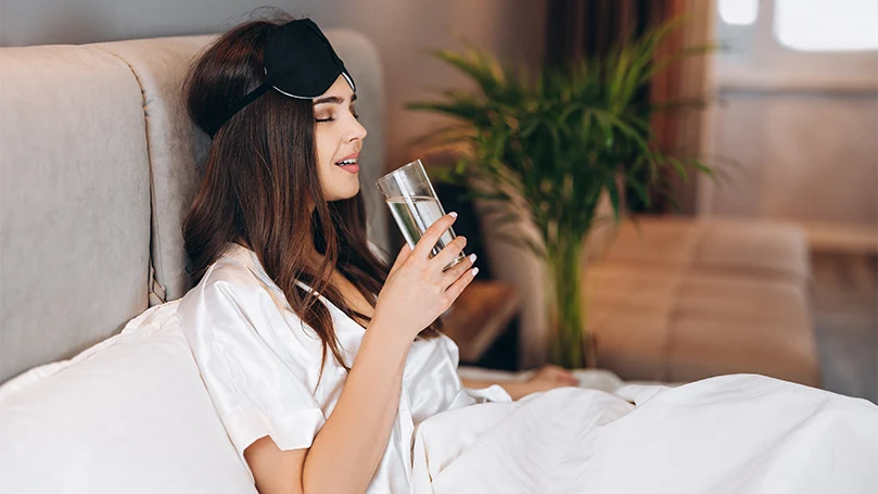 An image of a young woman drinks a water before going to sleep.