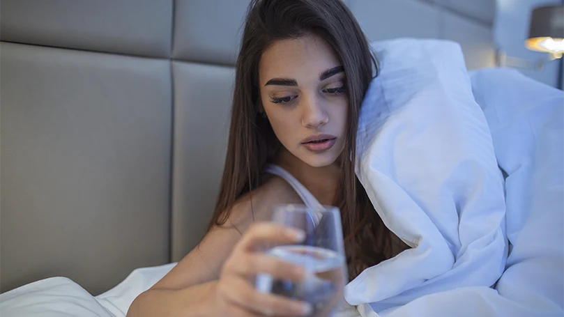 An image of a young woman having a glass of water in bed.