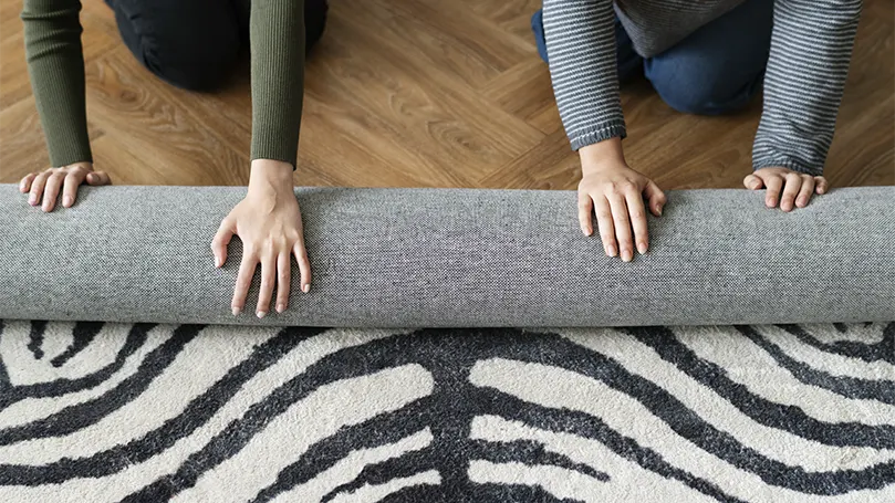 An image of a couple putting a rug uunder the bed to prevent it from sliding.