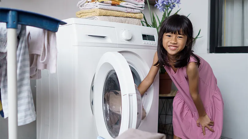An image of a little girl putting a blanket in a washing machine.