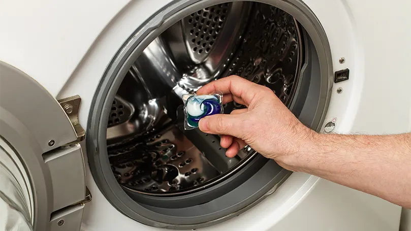 An image of a man putting a laundry pod in a washing machine.