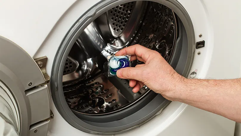 A man putting a laundry pod in a washing machine.