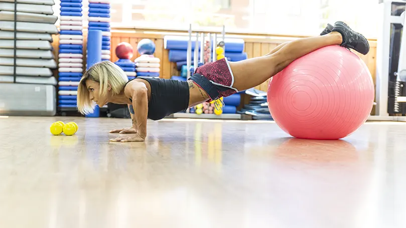 An image of a woman doing a Decline pushups on a yoga ball