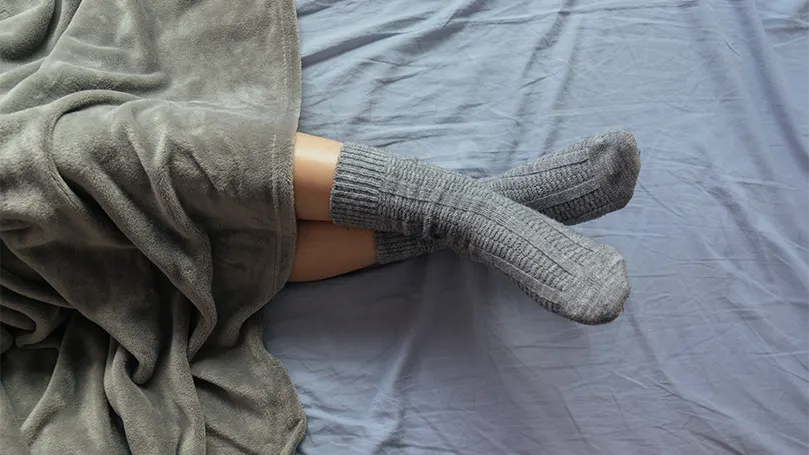 An image of a woman in bed with socks on her legs.